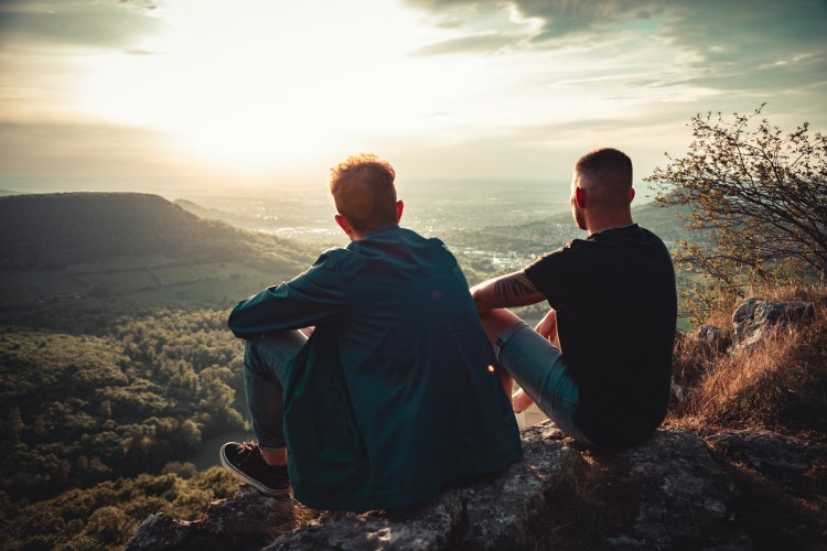 Two gay men gaze across a valley at sunset.